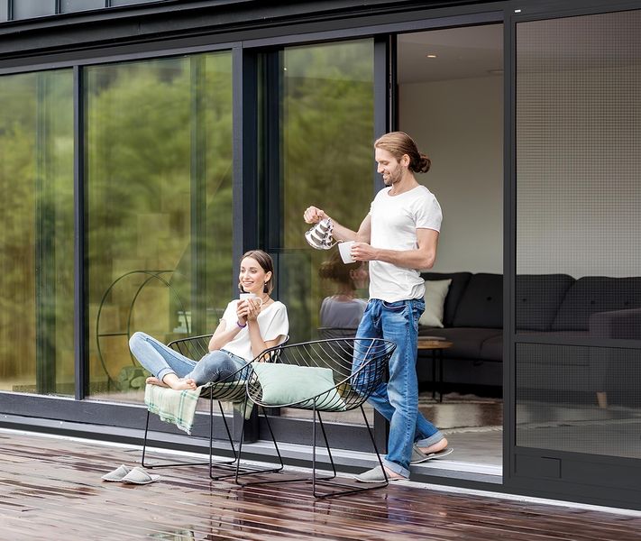 Paar auf moderner Terrasse mit schwarzem Insektenschutz-Schiebetürrahmen vor großflächiger Glasfront